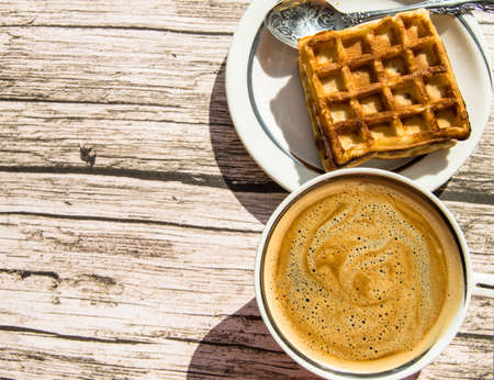 Soft Viennese waffle on a plate, a Cup of coffee on a wooden background, top view, copy space, flat lay.の写真素材