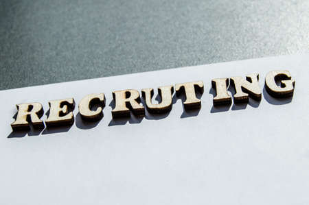 The word recruiting is written in wooden letters on a white background, the concept of hiring employees, recruitment in business and army.の写真素材