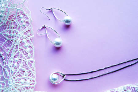 Beautiful silver shiny pearl jewelry with trendy neon glow, trendy glamorous earrings, chain on pink purple background with exquisite lace. Flat lay, top view, copy locationの写真素材