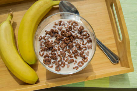 Bowl of oatmeal chocolate flakes in the shape of letters of the alphabet with milk on a wooden tray with bananas, healthy Breakfast concept for children and adultsの写真素材