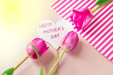 Flat lay composition with flowers and heart for mother's Day, greeting for women. Red tulips on pink background.の写真素材