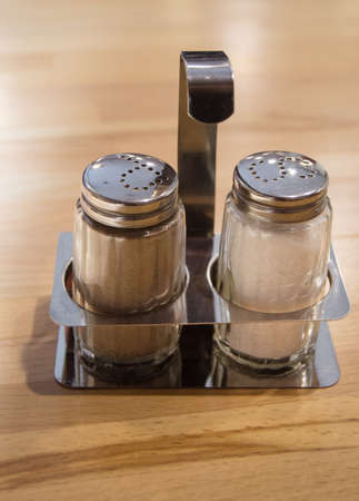 Glass and metal salt and pepper shaker set on wooden table in cafe, close up, vertical frame