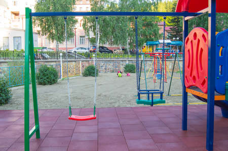Close-up of empty colorful plastic baby swing on Playground in Park on summer day.