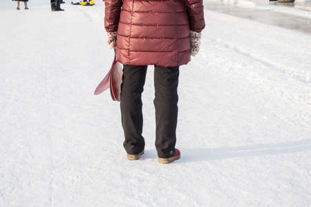 The view from the back of a woman in winter clothes standing in the snow in the Park and holding a...