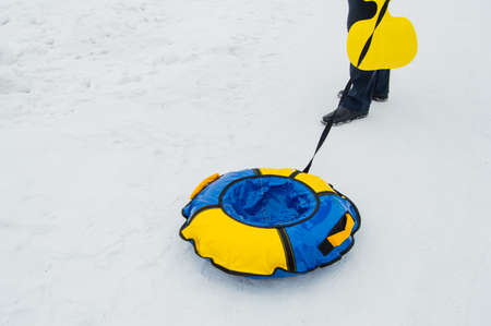 mens feet, the rope that pulls an inflatable rubber tubing in the snow for skating with ice slides in the winterの写真素材