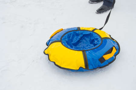 mens feet, the rope that pulls an inflatable rubber tubing in the snow for skating with ice slides in the winterの写真素材