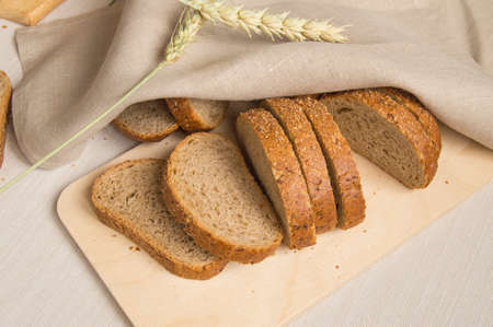 Fresh bread on a wooden chopping Board, wrapped in linen cloth, next to wheat ears, copy space, top view. Brown whole grain sliced bread, rustic background.の写真素材