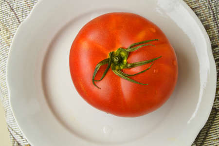 One large red ripe raw tomato on a white plate. Top view, the concept of organic food.