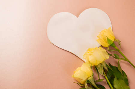 Paper heart with place for text and three yellow roses on a soft pink background view from above with copy space. Valentines day holiday conceptの写真素材