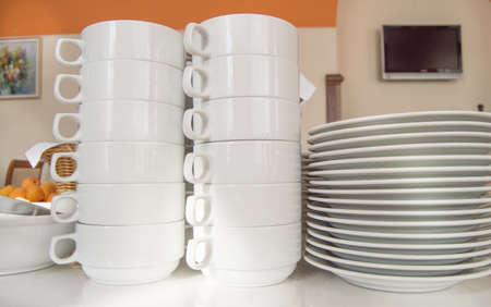 Close-up of a group of white ceramic tea cups and plates standing on a table with a white tablecloth, clean dishes in the hotel restaurant prepared for the guests ' Breakfast.の写真素材