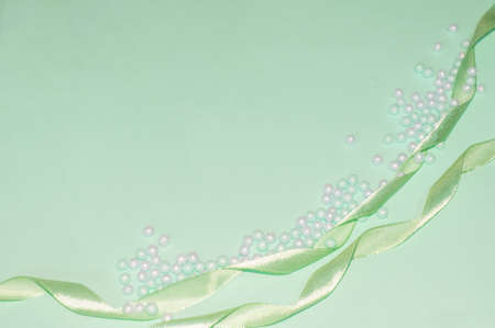 Layout with a spring green background, satin ribbon and beads for the design of the cards. Copy space.The concept of the celebration. Flat layout. The view from the top.の写真素材