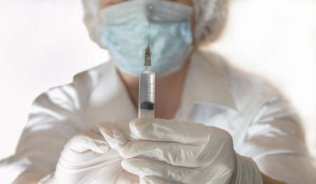 A doctor in medical gloves with a syringe is preparing for an injection. Focus on the syringe, vaccination for the prevention and treatment of viruses.の写真素材