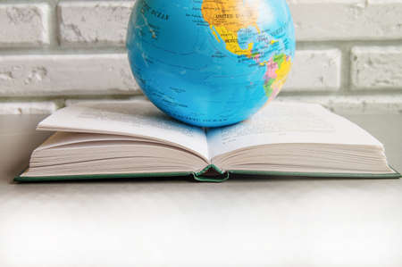 Close-up of a book open on a library table books and a globe, against a brick wall in the classroom, sunlight, the concept of world book dayの写真素材