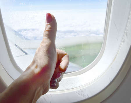 Close-up of a thumbs-up gesture, OK sign, a woman's hand on the background of a window in an airplane.の写真素材