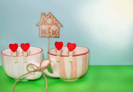 Two cups in blue and pink, tied with rope, red clothespins with hearts and a wooden house. The concept of a strong family with a copy of the space felt hearts.の写真素材
