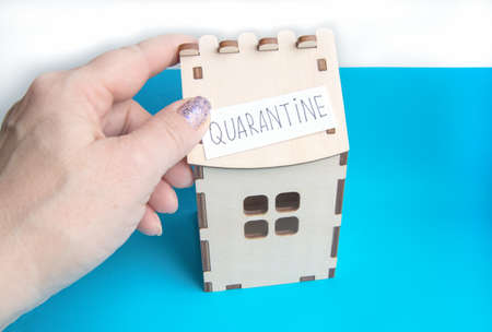 A woman's hand holds a piece of paper with the word Quarantine over a wooden house, A concept for preventing coronavirus disease with a COPY of the SPACE.の写真素材