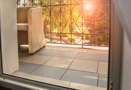 View from the room to the terrace or balcony with a metal railing. The sun shines through a transparent curtain and trees during sunset.の写真素材