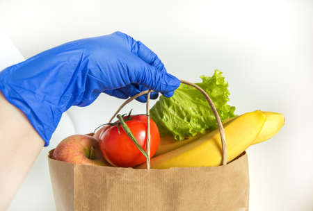 A hand in a rubber glove holds a paper bag with vegetables and fruits, food delivery in eco-friendly packaging, zero waste.の写真素材