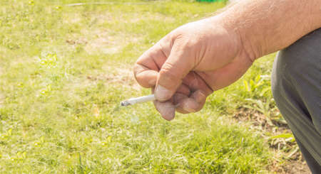 Close-up of an elderly man's hand holding a cigarette and Smoking against an open nature bokeh. Concept of harm of Smoking, Smoking cessation.の写真素材