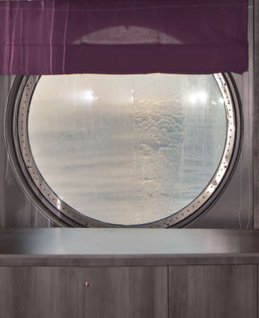 Round porthole of a sea cruise ship with water jets outside. Concept of sea travelの写真素材