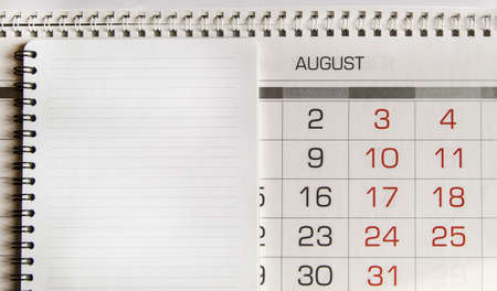 Top view of an August paper calendar and a blank page of a spiral-bound notebook as a time...