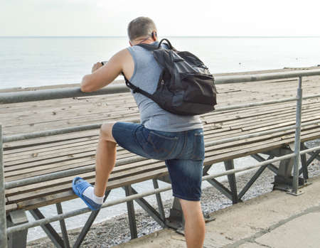 Man traveler with a backpack relaxing open sea, watching the dawn, leaning on the parapet, the...