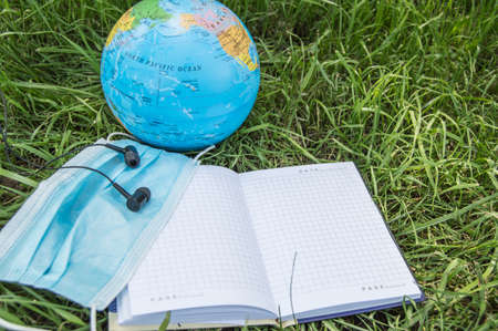 Medical mask, headphones, open Notepad with a copy of space, globe on the green grass, top view....