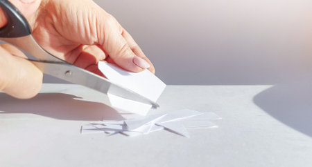 A woman's hand cuts a sheet of white paper with scissors and cuts off the corners. Close-up, DIY concept.の写真素材