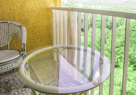 A comfortable seating area on the balcony with a rattan wicker chair, a transparent glass table and a rug, a home recreation concept.の写真素材