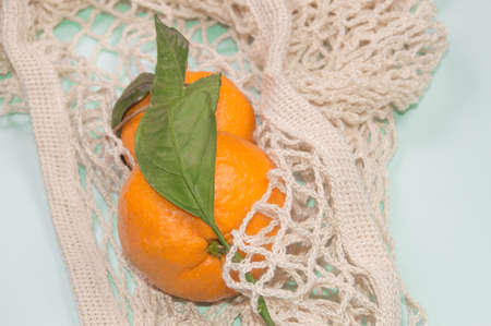 Ripe tangerines in a string bag on a blue background. Fruits in eco-friendly packaging.の写真素材