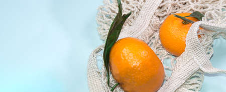 Blue banner background with tangerines in a string bag. Healthy lifestyle, top view, zero waste
