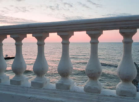 Classic white plaster balustrade on the background of a calm sea at sunset - a delicate pink moodの写真素材