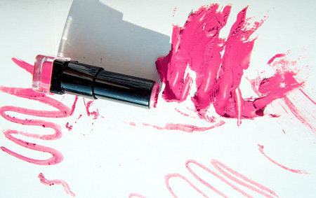 A tube of lipstick on smeared spots of red lipstick isolated on a white background. Creamy makeup texture and shadow. top view.の写真素材