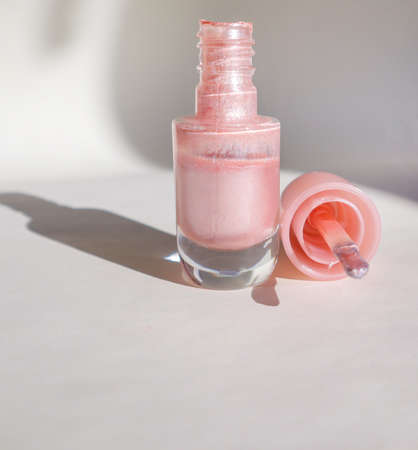 Top view of a bottle with pink nail polish and on a white surface with a shadow, the concept of...