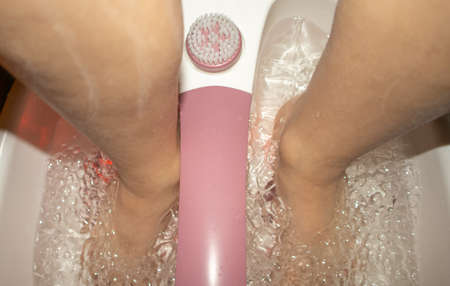 Close-up of feet in a tub with a vibrating foot massager. Electric foot massage bath and water bubbles. Pedicure and foot care.の写真素材