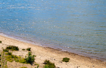 Sandy river bank with grass, coastline with blue water, top view.の写真素材