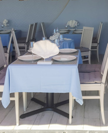 Beautiful table setting with glasses, tablecloth, plates in a nautical style in a fish restaurant, blue tinted.の写真素材