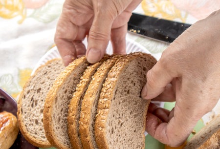 Womens old hands hold slices of whole grain bread with sesame seeds, close-up, selective focus.の写真素材