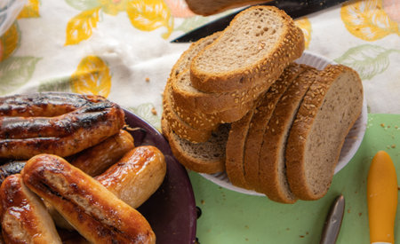 Slices of sesame bread, grilled sausages on a plate, rustic dinner on the table with a tablecloth.の写真素材