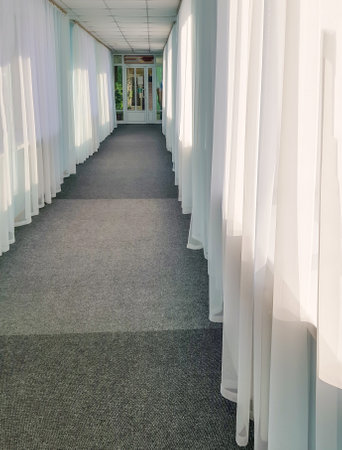 The prospect of a long hotel corridor with transparent curtains on large windows and glass doors.の写真素材