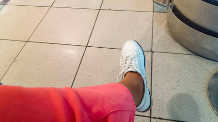 Women's legs in pink trousers and white shoes, carefree rocking, sitting in the airport waiting...