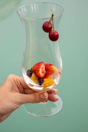 A summer cocktail with strawberries, cherries and foamy champagne in a woman's hand, against a blue pool backdrop. Party concept, vertical.の写真素材