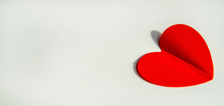 Banner with paper decoration in the shape of a red heart on a white background. Flat plan, top view, space for text on the left side.の写真素材