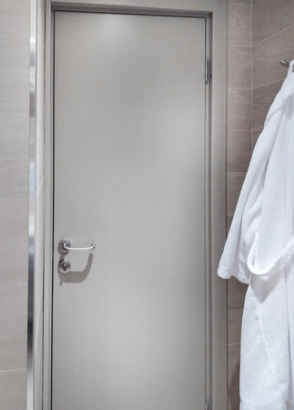 Closed hotel bathroom door, white bathrobes hanging nearby.の写真素材