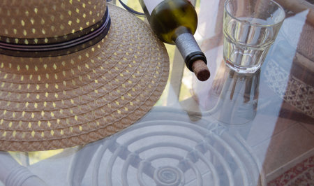A woman's summer hat, an empty wine bottle and a glass on a clear glass table on the balcony. Vacation concept.の写真素材