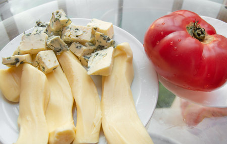 Different kinds of cheese on the plate and one red tomato, appetizers.の写真素材