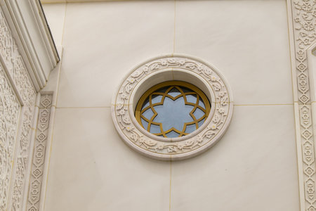 A round window with floral ornamentation and a carved frame on the white marble wall of the mosque.の写真素材