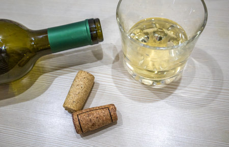 White wine in glass and open bottle with corks on light table, horizontal composition.