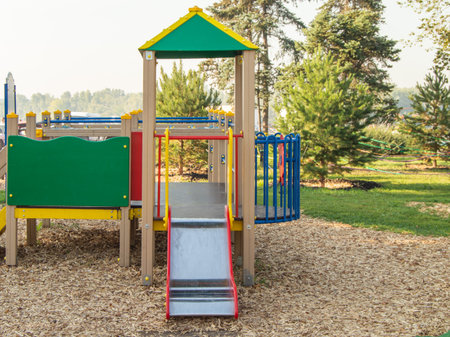 Modern colorful play structure with slide, metal chute, wood chip surfacing, green lawn and trees....