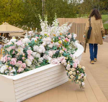 Decorative boat planter with pastel flowers on a deck by the water. A woman walks nearby. Romantic...